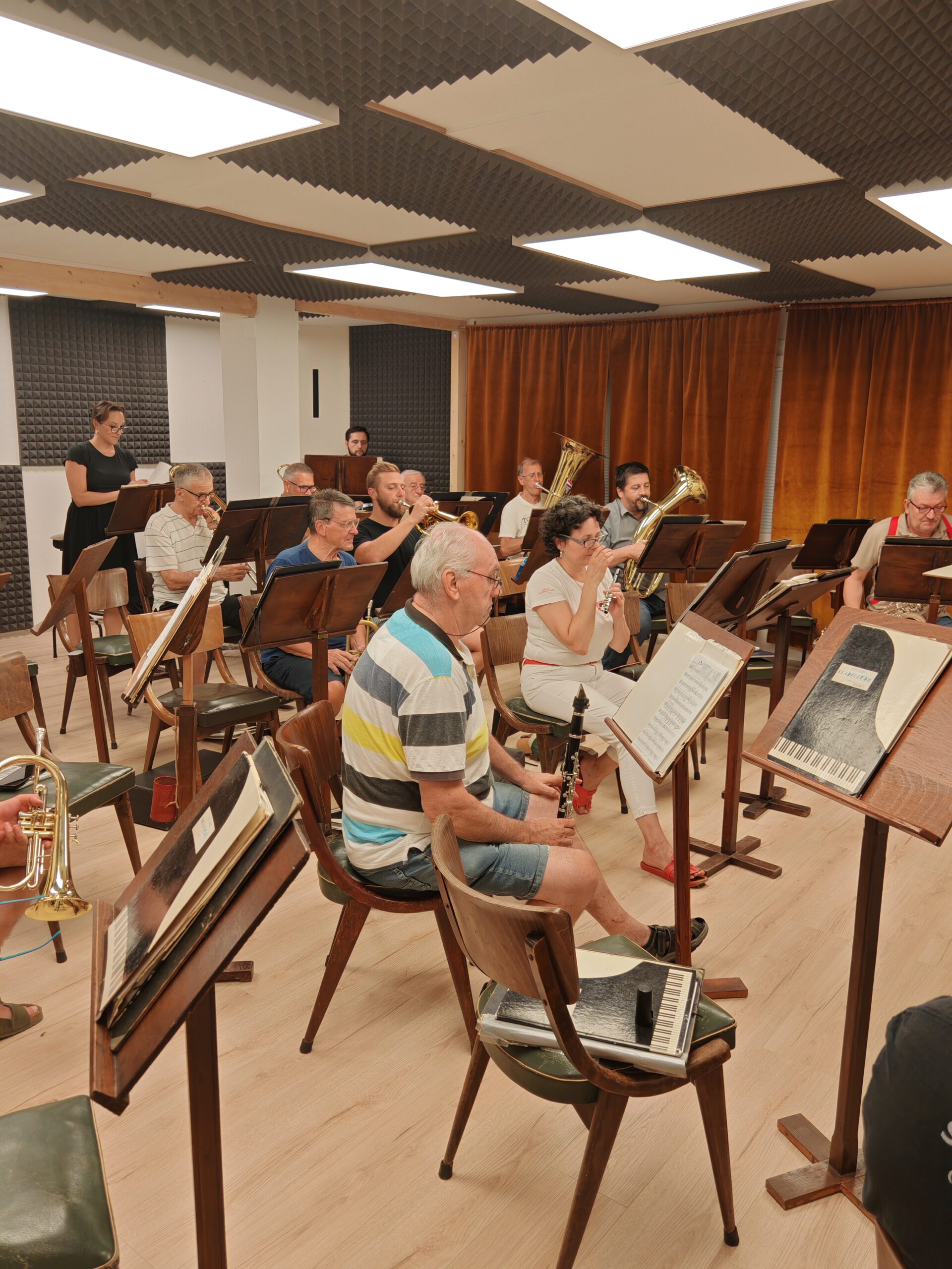 Članovi orkestra sviraju za notnim pultevima u novoj dvorani, u pozadini akustična obloga i zavjesa